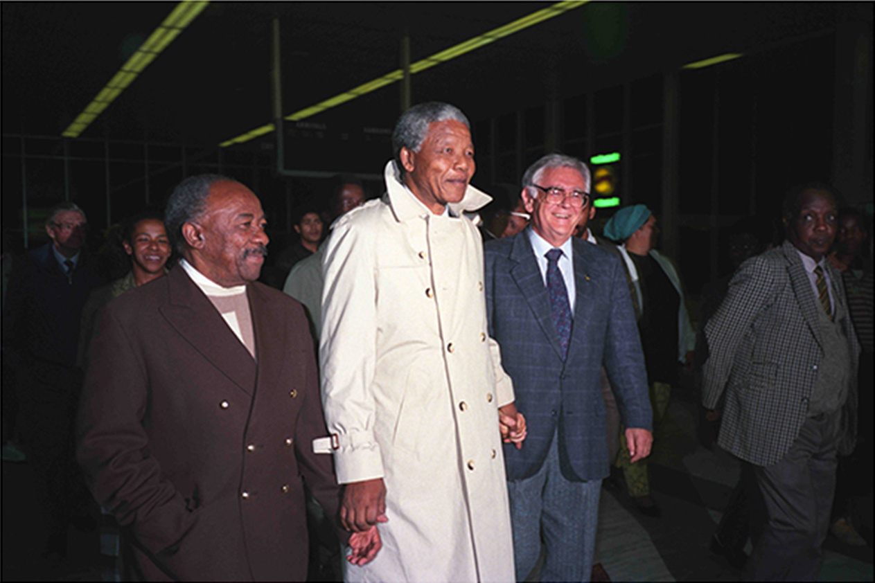 Nelson Mandela é ladeado por Alfred Nzo e Joe Slovo no aeroporto de DF Malan para dar boas-vindas aos exilados recentemente retornados de ANC e de SACP (Foto: Martyrs, saints & sell-outs/Divulgação)