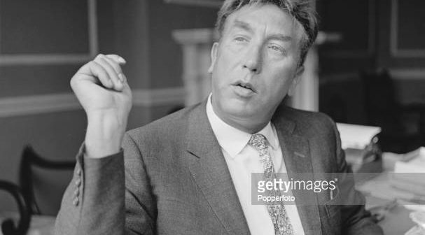 O comediante e ator inglês Frankie Howerd (1917-1992) sentado em uma mesa em casa em julho de 1966. (Foto de Popperfoto via Getty Images)