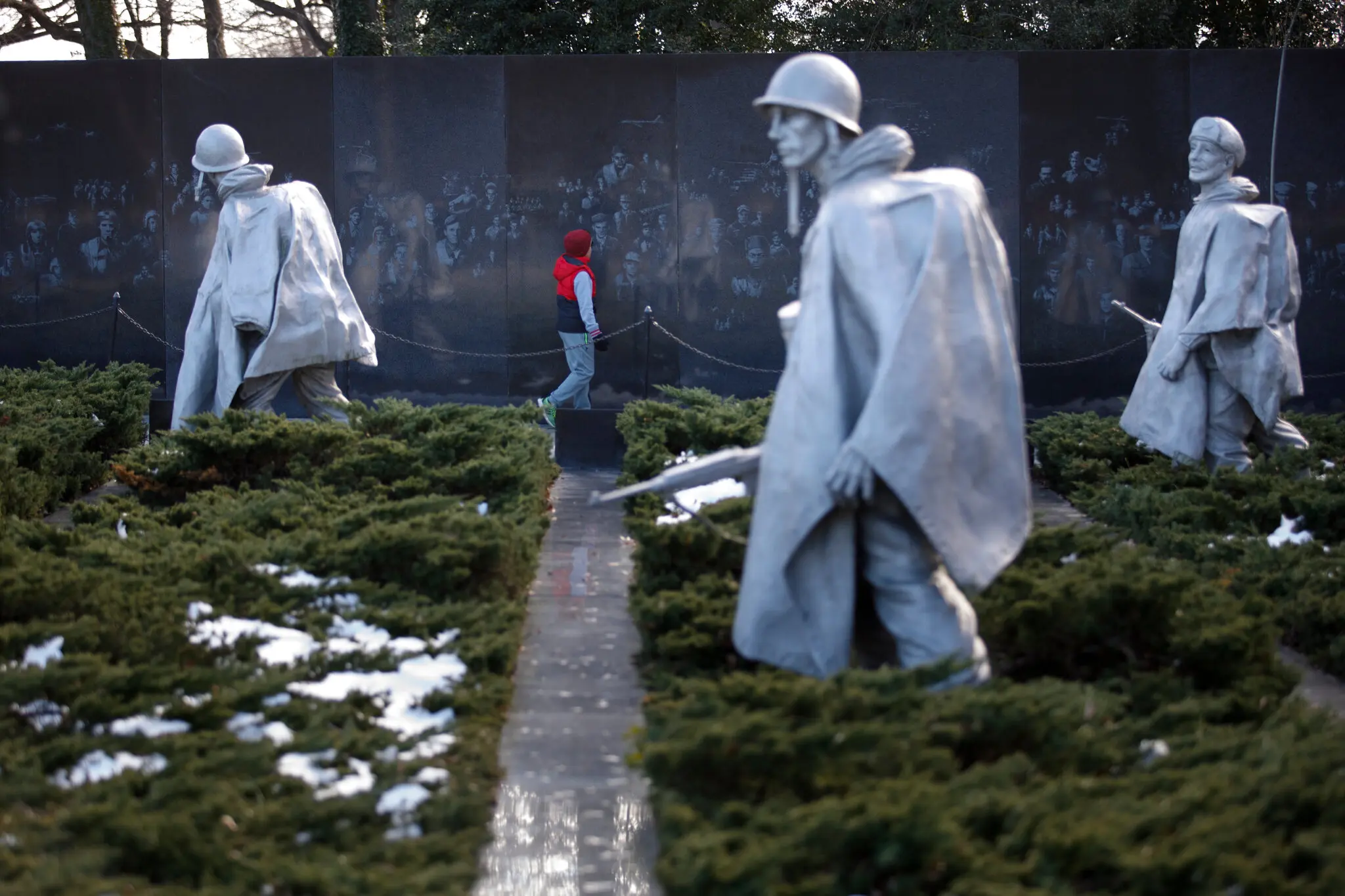 Três dos 19 soldados vestidos com ponchos esculpidos por Frank Gaylord em frente ao mural do Sr. Nelson.Crédito...Tom Brenner para o The New York Times