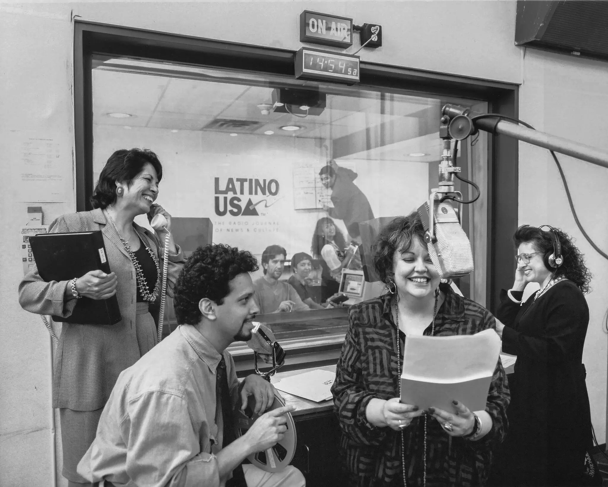 Maria Emilia Martin, atrás do microfone, em 1995, com outros membros da equipe do “Latino USA”, o programa de rádio público que ela criou em 1993.Crédito...Tommy Holt/Fotografia do Terceiro Olho