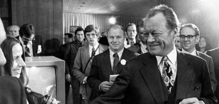 Sr. Binder, caderno na mão, atrás de Willy Brandt, o chanceler da Alemanha Ocidental, após a reeleição do Sr. Brandt em 1972. Entre os muitos livros que o Sr. Binder escreveu estava “The Other German: Willy Brandt's Life and Times”, publicado em 1976.Crédito...Agência de Imprensa Alemã