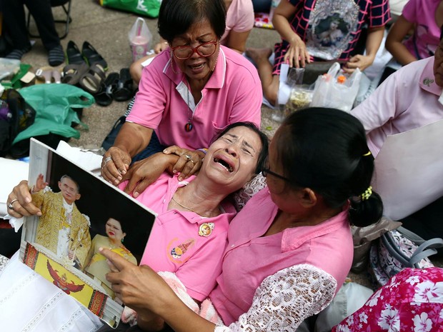 Mulher chora com uma foto do casal real da Tailândia na mão e é amparada por amigas em meio a um grupo acampado no hospital Siriraj, fazendo orações pelo rei Bhumibol Adulyadej, onde ele estava internado em Bangkok (Foto: Athit Perawongmetha/Reuters)