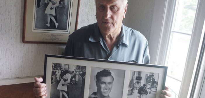 In this July 2, 2009, photo George Mendonsa poses for a photo in Middletown, R.I., holding a copy of the famous Alfred Eisenstadt photo of Mendonsa kissing a woman in a nurse's uniform in Times Square on Aug. 14, 1945, while celebrating the end of World War II, left. Mendonsa died Sunday, Feb. 17, 2019, he was 95. It was years after the photo was taken that Mendonsa and Greta Zimmer Friedman, a dental assistant in a nurse’s uniform, were confirmed to be the couple. (Connie Grosch/Providence Journal via AP)