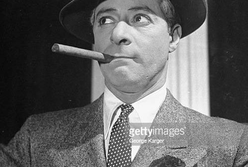 O comediante George Jessel, de chapéu e fumando charuto, parecendo indignado, na peça Show Time. (Foto de George Karger/Getty Images)