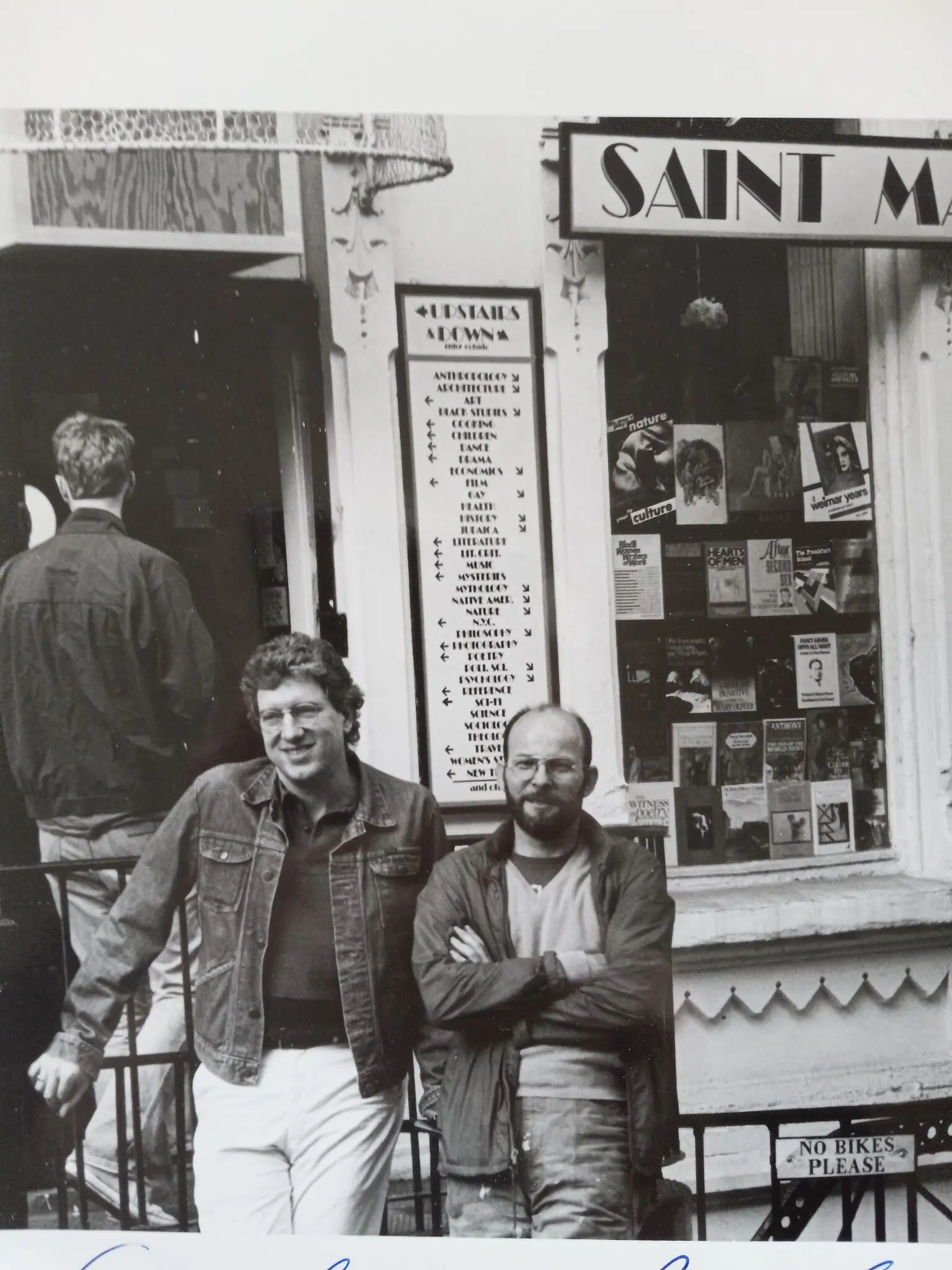Bob Contant, à esquerda, com Peter Dargis, outro proprietário da Livraria São Marcos, no início dos anos 1980. (Como a placa indica, a palavra “Santo” às vezes estava escrita no nome da loja, às vezes não.) (Crédito da fotografia: por Marilyn Berkman)