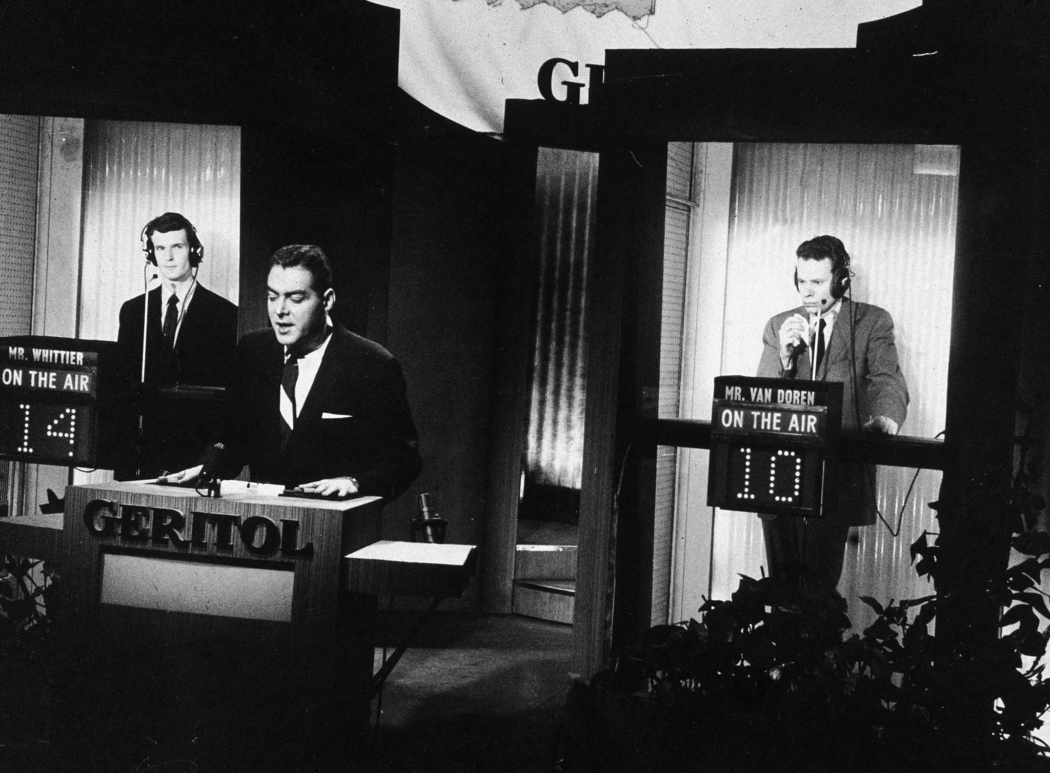 Charles Van Doren, à direita, no estande de um concorrente durante sua série de aparições em 1956 e 1957 no programa de perguntas e respostas “Twenty-One”. O anfitrião, no centro, era Jack Barry. O outro competidor foi Anthony Whittier. Mais tarde, Van Doren confessou ao Congresso que recebeu as respostas às perguntas. (Crédito da fotografia: Televisão NBC, via Getty Images)