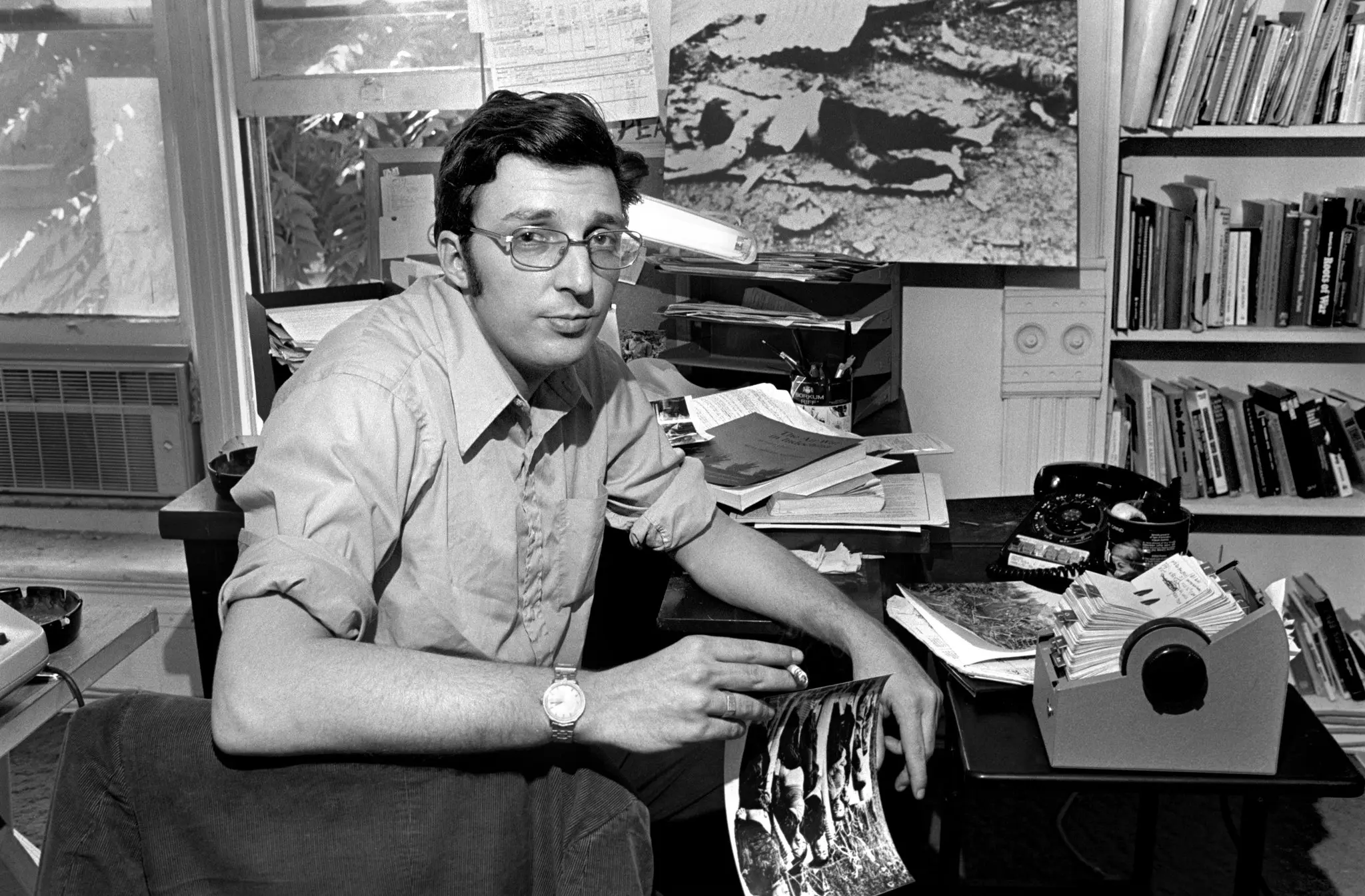 Fred Branfman em seu escritório em Washington com fotos dos danos e das vítimas dos bombardeios, em 1972. (Crédito da fotografia: Cortesia George Tames/The New York Times)