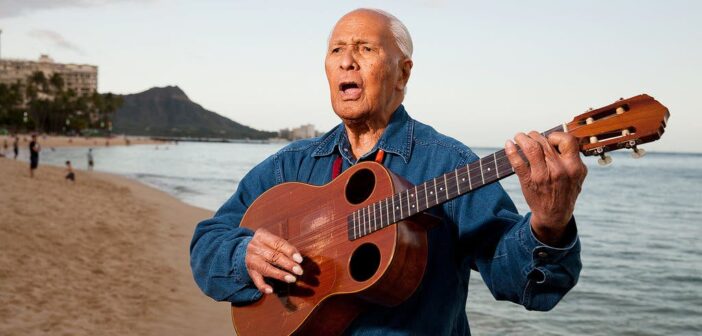 Eddie Kamae tocando um ukulele barítono que ele chamava de “guitarra ukulele”, na praia de Waikiki.Crédito...Marco Garcia