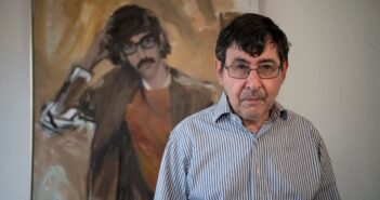 O poeta e historiador de arte David Shapiro em 2018, em frente a uma pintura sua, muito mais jovem, de seus dias de estudante na Universidade de Columbia.Crédito...Michael Karas/USA Today Network