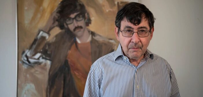 O poeta e historiador de arte David Shapiro em 2018, em frente a uma pintura sua, muito mais jovem, de seus dias de estudante na Universidade de Columbia.Crédito...Michael Karas/USA Today Network